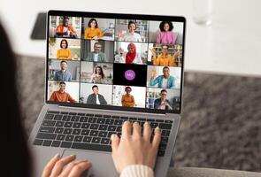 Woman using a laptop to participate in an online chat meeting. The screen displays several participants in a grid format, showcasing a diverse group of people. photo