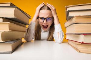 Back To School Stress. Little Girl Shouting Clutching Head Sitting Between Two Book Stacks On Yellow Studio Background. photo
