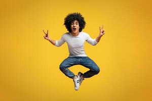 Enjoy your life. Happy joyful african-american man jumping up in air, demonstrating v-signs, orange studio background photo