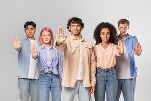 Five diverse individuals, including two men and three women, standing together in front of a grey background, looking at the camera and have their hands raised in a gesture of resistance or refusal photo