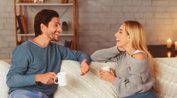 Happy Couple Spending Time Together Drinking Tea And Talking Sitting On Sofa At Home. Selective Focus photo