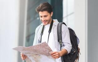 Happy Tourist. Smiling Young Man Standing Near Airport With City Map In Hands, Checking His Route, Empty Space photo