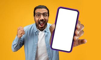 Indian man is holding up a cell phone in his hand, and his face displays a surprised expression. It seems that he has received unexpected news or seen something shocking on the screen. photo