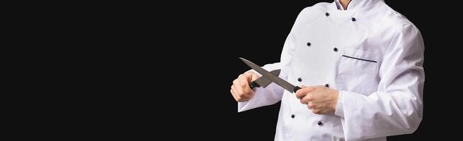 Professional Chef. Funny Cook Guy Sharpening Knives Posing In Studio Over Black Background. Panorama, Free Space For Text photo