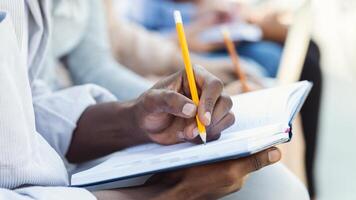 Cropped of black student guy taking notes, studying with friends, using notepad and pencil photo
