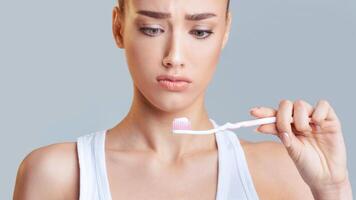 The image features a close-up portrait of a young woman holding a toothbrush with toothpaste on it. She is looking down at the toothbrush with a slightly worried expression on her face. photo