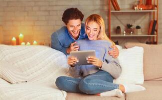Weekend. Relaxed Spouses Browsing On Tablet Computer Browsing Internet Or Watching Movie Sitting On Sofa At Home. Selective Focus photo