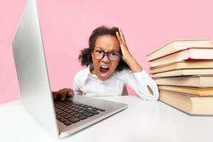 School Overload. Black Elementary Student Girl Sitting At Laptop And Screaming Doing Homework. Yellow Background, Studio Shot photo