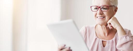 Smiling beautiful senior woman using digital tablet at home, empty space, close up photo