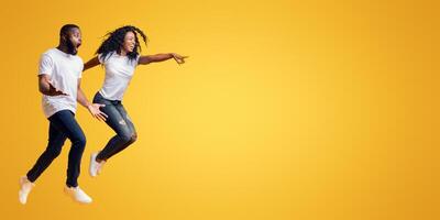 Surprised Black Man Is Looking At Free Space, afro woman is jumping and pointing at empty space, yellow background, panorama photo