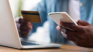 Online payment. Unrecognizable black man holding credit card and using smartphone for shopping in internet at workplace, selective focus on device photo
