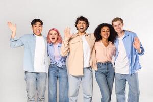 A group of five young adults, representing diverse ethnicities and genders, stand together against a white background. They are all smiling and appear to be happy and friendly. photo