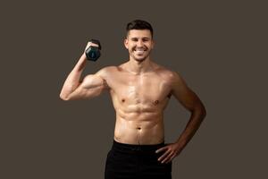 A man is standing and posing while holding a dumbbell in his hand. He is showcasing his muscles and strength, with a focused expression on his face. photo