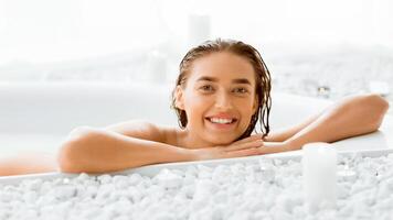 Tender woman having soothing bath with foam, relaxing and smiling to camera photo