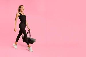 Smiling Fitness Lady Going To Gym Carrying Bag With Rolling Mat On Yellow Studio Background. Full Length photo