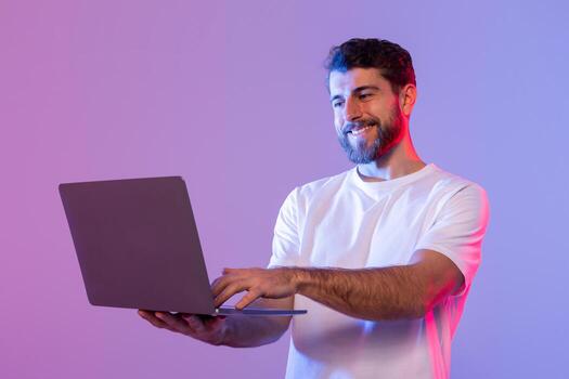 un hombre en un blanco camisa es en pie y participación un ordenador portátil en su manos. él aparece enfocado en el pantalla, posiblemente trabajando o estudiando. el antecedentes es sencillo y vacío de ninguna distraer elementos. foto