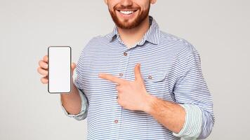 Cropped of smiling man holding latest slim cellphone with white empty screen and pointing at it, free space, mockup photo
