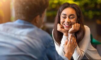 African American guy and girl are engaged in conversation at a table in a restaurant. Both individuals appear to be attentive to each other, leaning in slightly as they speak. photo
