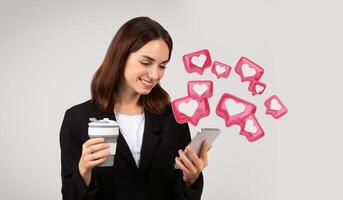 Multitasking millennial caucasian businesswoman in a stylish black suit browsing her smartphone with a smile while enjoying a hot beverage, texting her lover photo