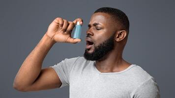 Picture of a young black man having an asthma attack, using inhaler over white background photo