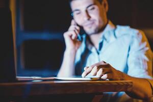 Unrecognizable Businessman Using Digital Tablet And Business Application Talking On Cellphone Working Indoors At Night. Selective Focus photo