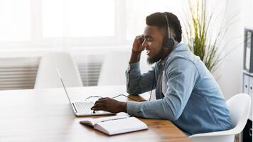 Customer support concept. Black millennial manager with headset using laptop in office, solving client's issue. photo