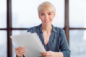 Businesswoman Working With Papers And Documents Sitting At Workplace And Smiling To Camera In Modern Office. Entrepreneurship And Business Accounting photo
