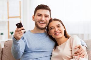 Weekend. Happy Couple Watching TV Relaxing Sitting On Sofa At Home. Selective Focus, Copy Space photo