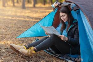 Young girl checking map in camping tent, hiking in autumn forest, empty space photo