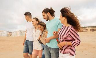 A group of five friends walks together along the beach, engaging in cheerful conversation. The sun is setting, casting a warm glow on their relaxed outing. photo