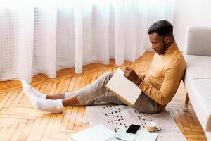 Afro Student Guy Taking Notes Preparing For Lecture Or Exam Studying Sitting On Floor At Home. Selective Focus photo