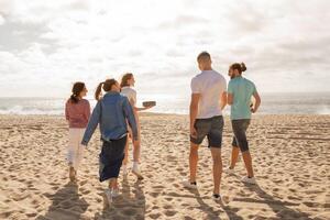A group of friends walks along the sandy beach, laughing and enjoying the warm sunlight. One person is about to throw a frisbee, creating a lively atmosphere by the ocean. photo