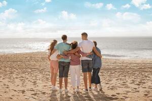 A group of five people stands together on a sandy beach, overlooking the ocean. They share a moment of connection as they enjoy the warm sunlight and gentle waves in the background. photo
