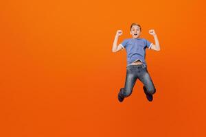 Winner. Expressive excited boy enjoying success in moment of jumping in air, orange studio background photo