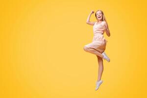 Overjoyed young woman jumping in the air, celebrating success with raised fists over yellow studio background, full-length shot, free space photo