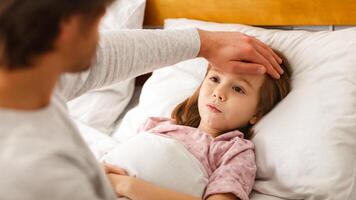 Man checking his ill little daughter temperature, touching his forehead, close up photo