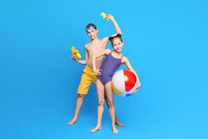 Happy summer holidays. Cheerful boy and girl playing with beach toys, blue studio background photo