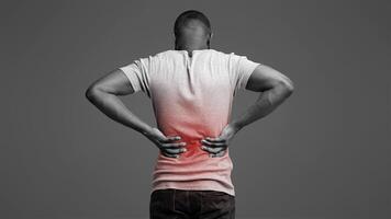 Afro guy holding both hands behind his back, pain in spine, inflamed zone highlighted in red, white background photo