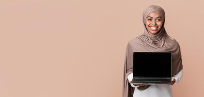 Cool Website. Smiling Black Muslim Girl In Hijab Holding Laptop Computer With Blank Black Screen For Mockup, Standing Over Yellow Background photo