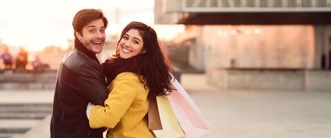 A couple smiles while walking with shopping bags in hand, enjoying their time on a bustling city street in autumn, copy space photo