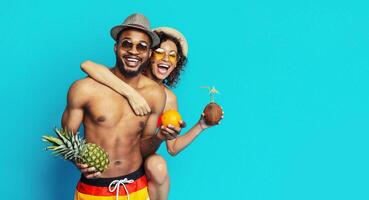 African American young couple posing playfully against a blue backdrop, enjoying a tropical theme. They are both smiling and seem to be having a great time, copy space photo