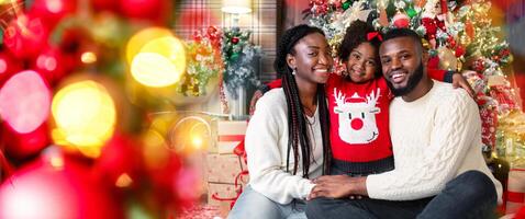 Merry Christmas and happy New Year. Portrait of afro dad, mom and daughter posing near Xmas tree at home photo