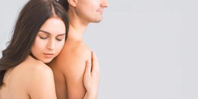 A woman with long dark hair is embracing a man from behind. She has her eyes closed and her head resting on his shoulder. Both are bare-chested and appear to be intimate, copy space photo