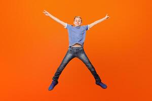 Happy school boy having fun, jumping on orange studio background photo