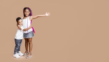 Portrait of lovely african american sister and brother posing together on yellow background in studio, cuddling and smiling. Copy space photo