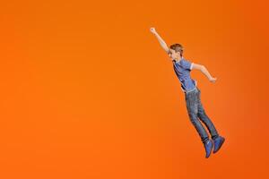 Little boy simulating flight, jumping with raised fist like superhero on orange background photo