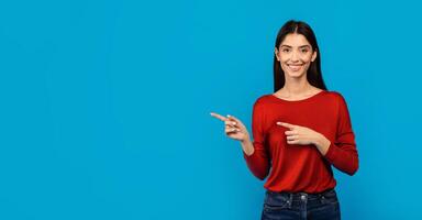 A woman wearing a red sweater is pointing at an unseen object off-camera, engaged and focused on whatever has caught her attention, her gesture suggesting significance or direction, copy space photo