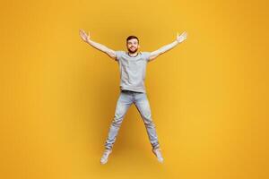 A man leaps energetically into the air, arms outstretched as if reaching for the sky in a moment of intense motion and freedom, yellow background photo