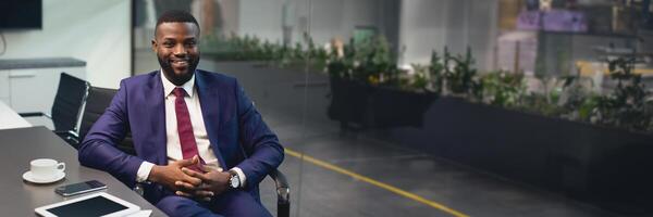 Handsome african american young businessman in nice suit sitting at table with documents, smartphone, digital tablet, drinking coffee at conference hall in office, having business meeting, copy space photo