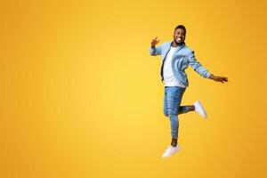 Portrait of funny black man jumping on yellow background with euphoric face expression, free space for text photo